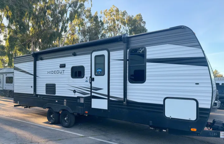 Side view of a white and black Keystone Hideout travel trailer RV rental with an extended awning, parked in a lot.. Keystone Hideout 2020