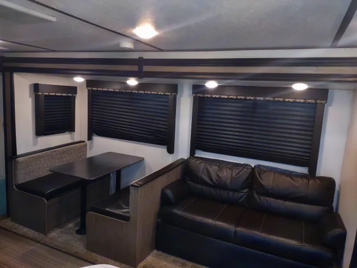RV rental interior: A cozy living and dining area with a dark leather sofa, booth seating, and blinds.. Keystone Hideout 2020