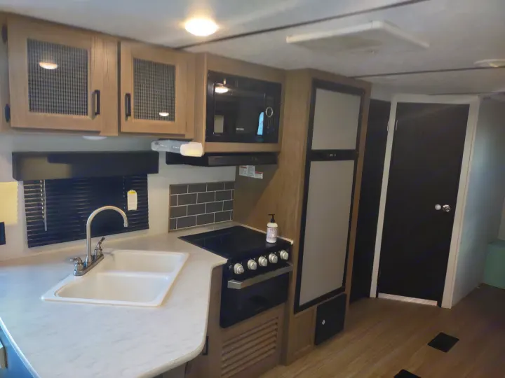 Modern RV rental kitchen featuring a sink, stove, microwave, and refrigerator. Essential amenities for your road trip comfort.. Keystone Hideout 2020