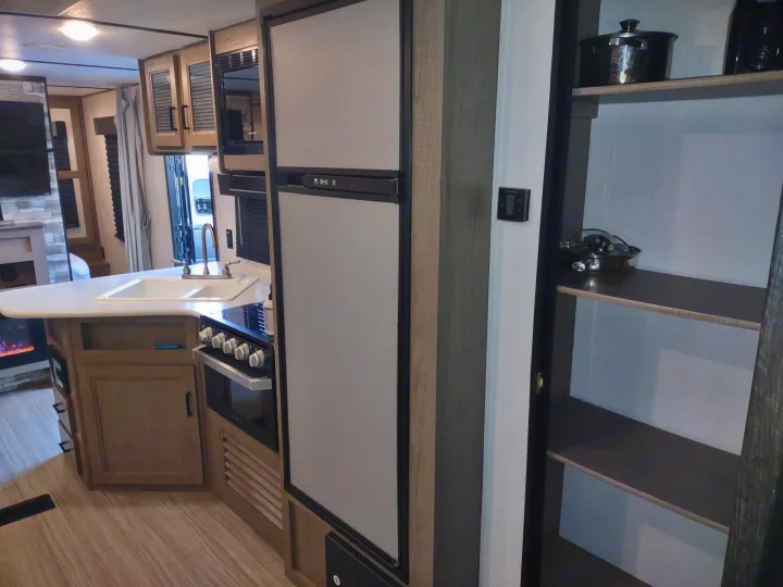 Inside an RV rental: a well-equipped kitchen with sink, stove, refrigerator, and an inviting living area.. Keystone Hideout 2020