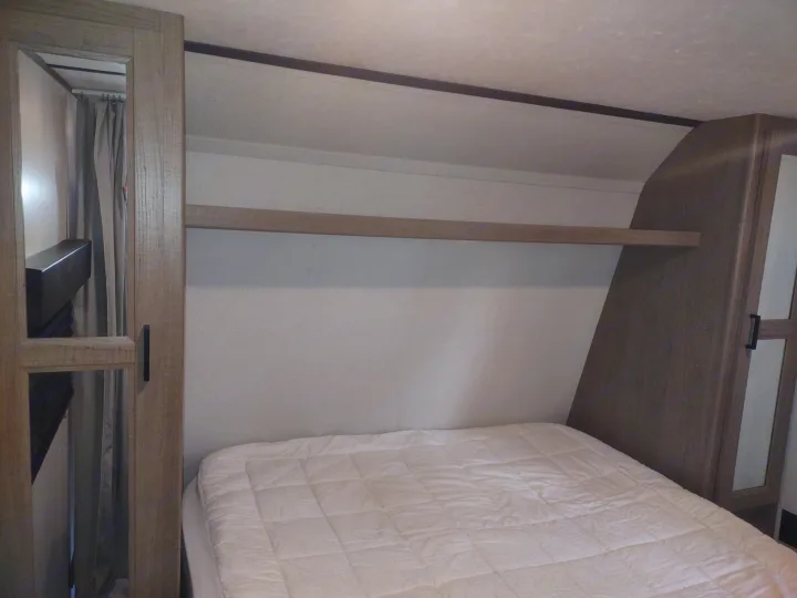 RV rental bedroom with a comfortable bed, overhead storage shelf, and mirrored wardrobes on each side.. Keystone Hideout 2020
