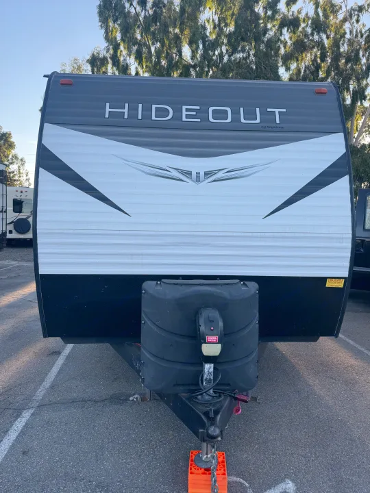 Frontal view of a white and black Hideout by Keystone RV rental travel trailer with its hitch and propane tanks visible.. Keystone Hideout 2020