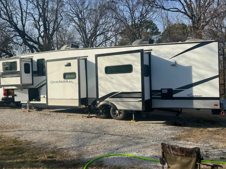 White RV rental (fifth wheel) with slide-outs extended, parked on gravel in a sunny campground. Ready for your next travel adventure.. Coachmen Chaparral 2021