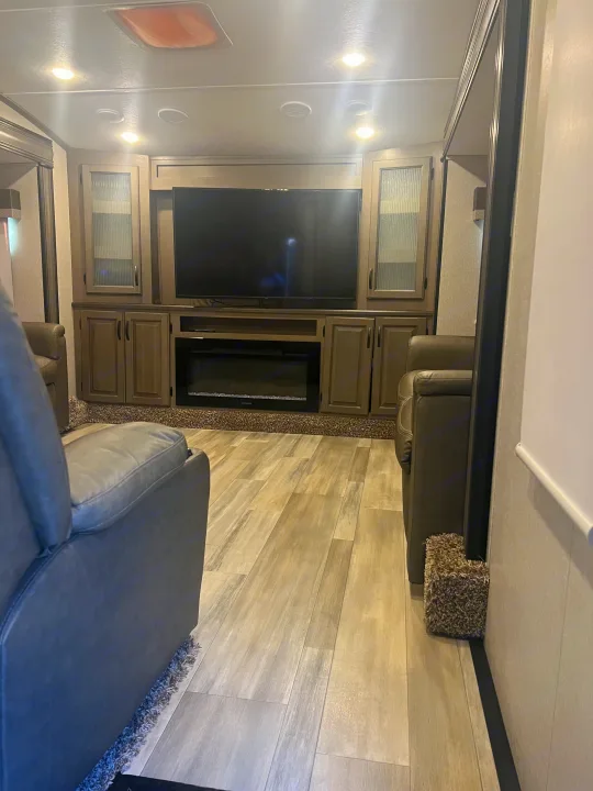 Spacious RV rental living area with large TV, electric fireplace, recliners, and stylish wood-look flooring.. Coachmen Chaparral 2021