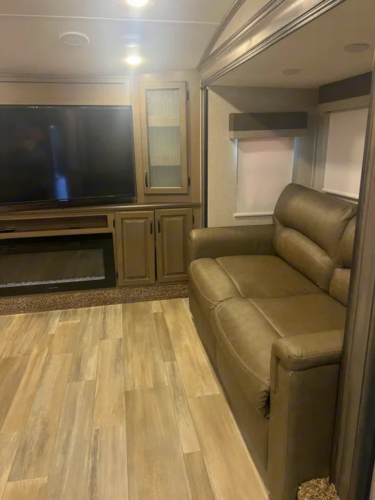 RV rental living room featuring a large TV, electric fireplace, cabinets, light wood-look floor, and a comfy sofa.. Coachmen Chaparral 2021