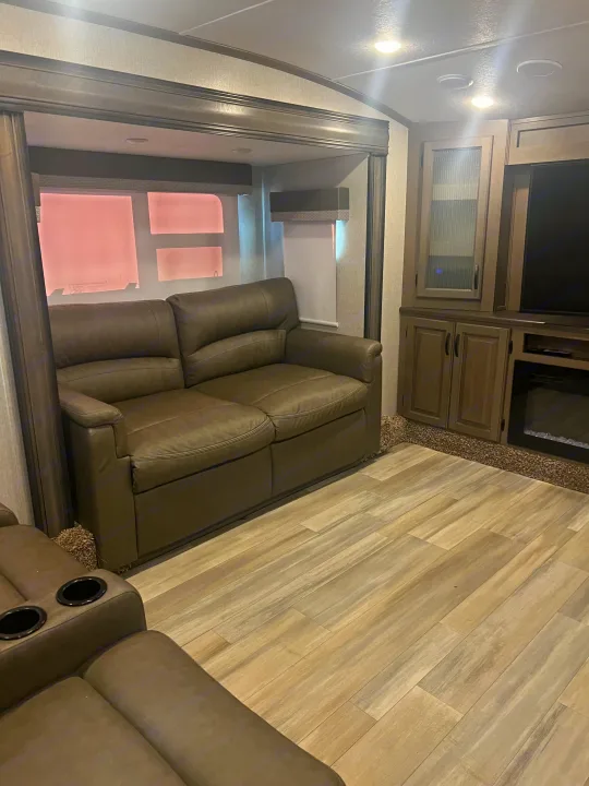 Enjoy this cozy RV rental living space featuring a leather sofa, built-in entertainment center, and sleek wood-look flooring. Includes cup holders.. Coachmen Chaparral 2021