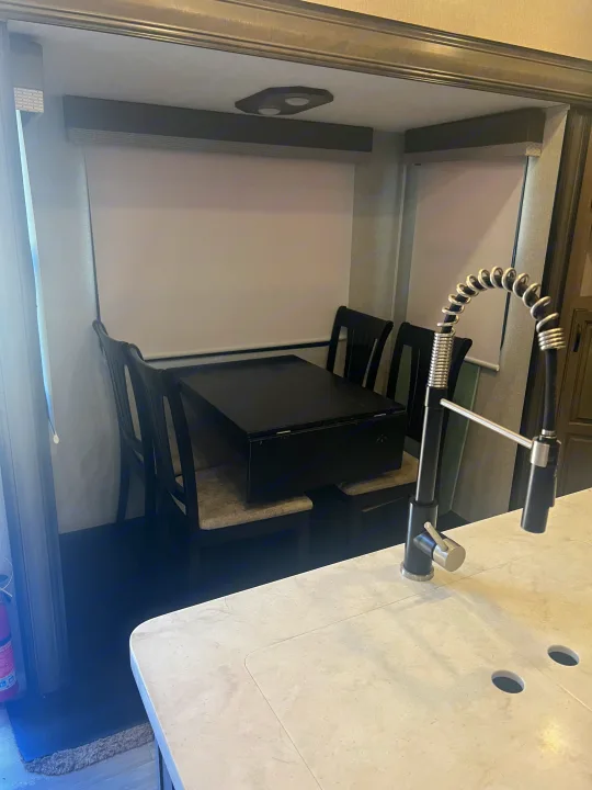 Compact RV rental dining and kitchen area, featuring a black table with four chairs and a modern sink faucet.. Coachmen Chaparral 2021