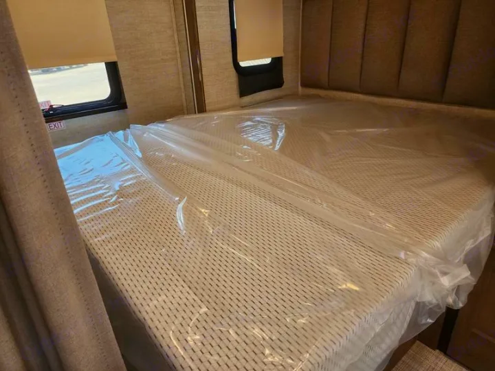 New RV rental bedroom featuring a mattress still in plastic, an 'EXIT' sign, and a window. Ready for your trip!. Entegra Coach Qwest 24L 2024