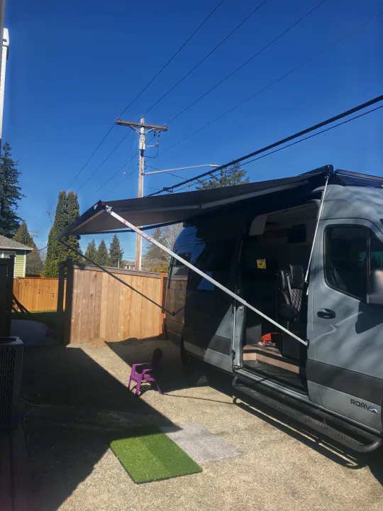 Gray RV rental camper van with extended awning, parked in a sunny yard. Ready for adventure!. Mercedes-Benz Sprinter 2022
