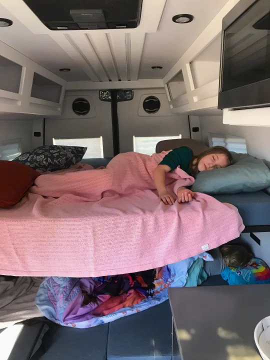 Peaceful sleep in an rv rental: child on bed, another below. Cozy travel van interior with overhead storage.. Mercedes-Benz Sprinter 2022