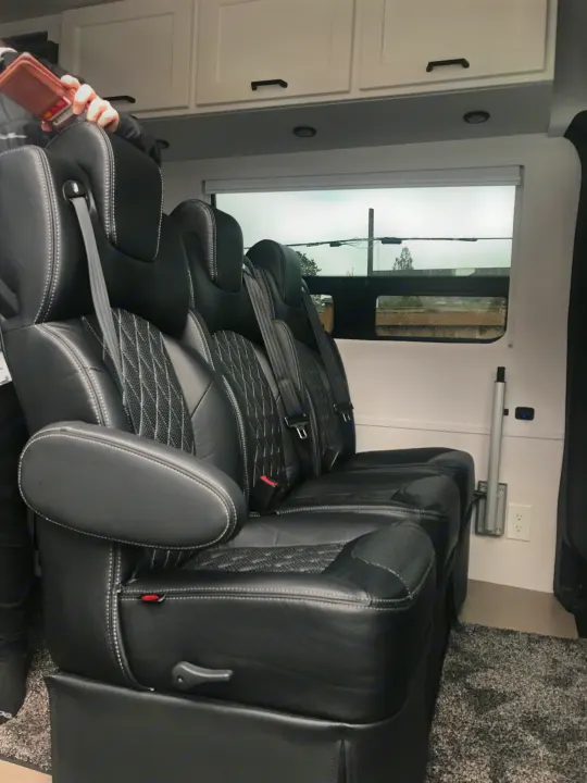 Luxury RV rental interior featuring plush black leather captain's chairs with white stitching, overhead cabinets, and a window view.. Mercedes-Benz Sprinter 2022
