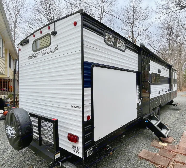 White and black Grey Wolf RV rental parked, showcasing its side profile, rear with spare tire, and entry steps.. Forest River Grey Wolf 29TE 2024