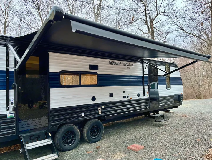 Grey Wolf travel trailer with extended awning, ideal for an **rv rental** adventure, parked on gravel in an outdoor setting.. Forest River Grey Wolf 29TE 2024