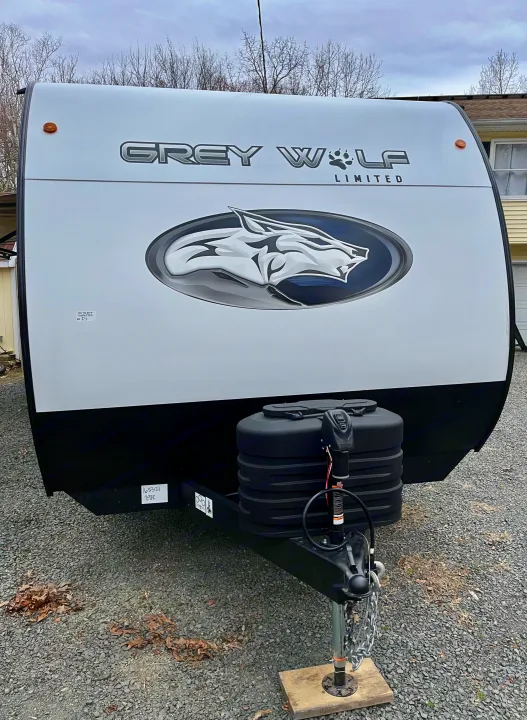 Front view of a white Grey Wolf travel trailer with a black base, featuring a bold wolf logo. Perfect for your next RV rental adventure.. Forest River Grey Wolf 29TE 2024