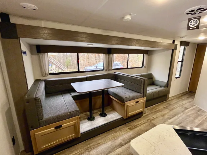 Modern RV rental interior showing a comfortable dinette with U-shaped seating, storage, and large windows with outdoor views.. Forest River Grey Wolf 29TE 2024