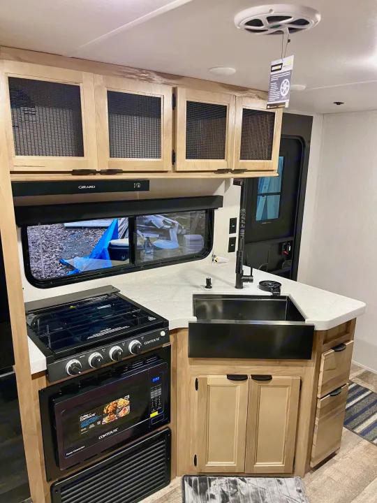 Spacious RV rental kitchen featuring light wood cabinets, black appliances, a modern sink, and ample counter space for travel.. Forest River Grey Wolf 29TE 2024