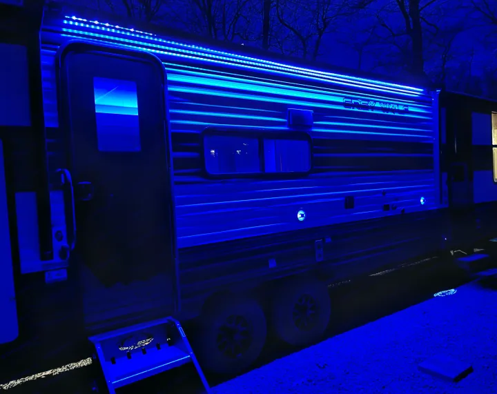 A stylish RV rental brilliantly lit with glowing blue LEDs at night, highlighting its side and steps.. Forest River Grey Wolf 29TE 2024