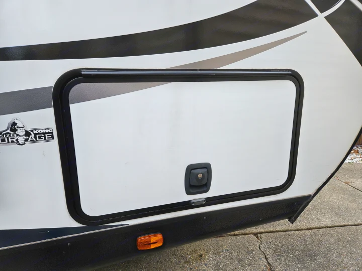 RV rental exterior showing a side storage compartment with a "Kong Storage" decal, black & grey stripes, and an orange marker light.. Heartland RVs North Trail 2021