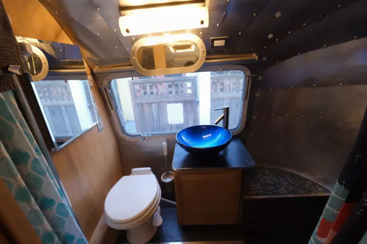 This cozy rv rental bathroom features a vibrant blue sink, toilet, and window view into the outside world.. Airstream Tradewind 1979