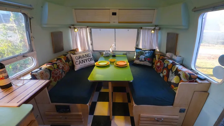 Step into this bright RV rental's cozy dinette! Features include a green table, vibrant floral cushions, and outdoor views.. Airstream Tradewind 1979