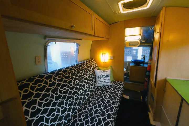 Cozy RV rental interior features a black-and-white patterned sofa with a humorous pillow, and a compact sink area.. Airstream Tradewind 1979