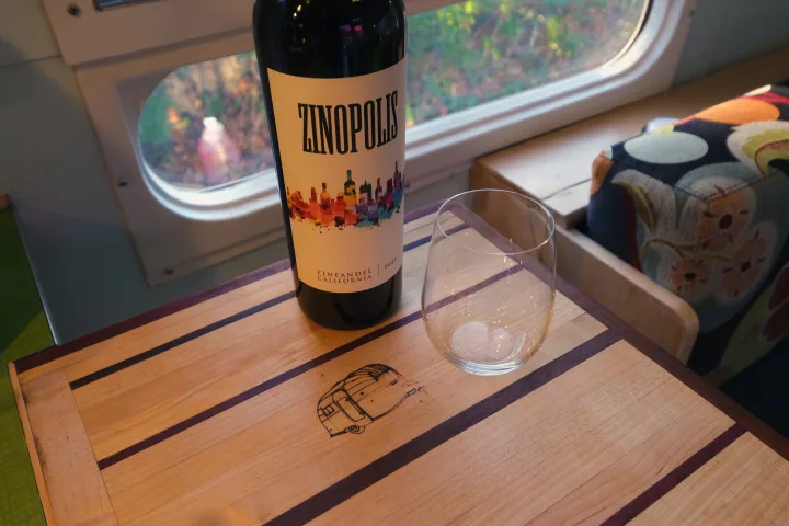 Unwind with ZINOPOLIS Zinfandel inside a comfy rv rental, featuring a unique camper-engraved table and window view.. Airstream Tradewind 1979