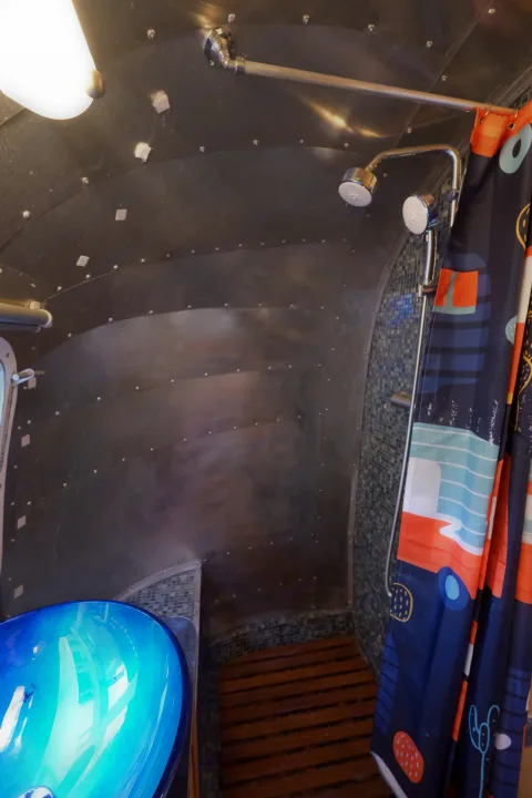 Step into this modern RV rental bathroom with sleek metal walls, dual showerheads, a bright blue sink, and a wooden floor.. Airstream Tradewind 1979