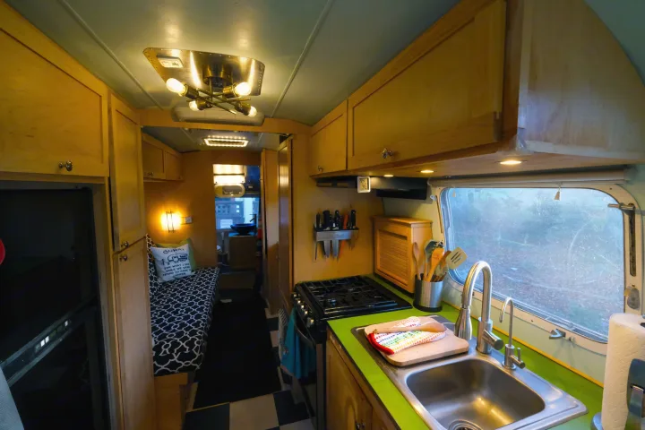 Cozy RV rental interior with full kitchen, dining nook/bed, wood cabinetry, and checkerboard floor.. Airstream Tradewind 1979