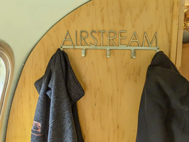 Inside an RV rental: a custom "AIRSTREAM" coat rack mounted on a wooden wall, holding two jackets.. Airstream Tradewind 1979