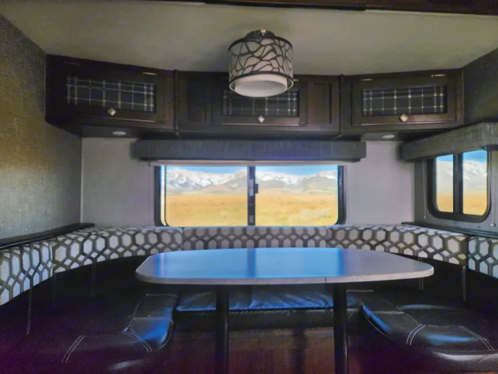 Inside a comfortable rv rental: dinette with patterned seats, overhead storage, and stunning mountain scenery.. Heartland Wilderness 2019