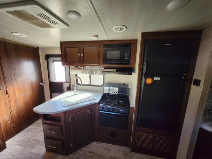 Step inside this RV rental's full kitchen: sink, gas stove, microwave, and large refrigerator within wood cabinetry.. Heartland Wilderness 2019
