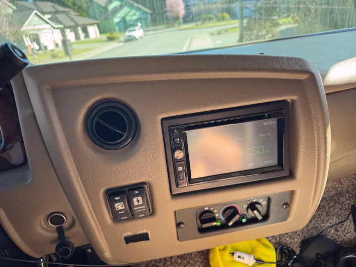 Interior view of an RV rental dashboard: Jensen radio (87.50 MHz), climate, and generator controls.. Flair-Fleetwood Flair-Fleetwood Motorhome 2017