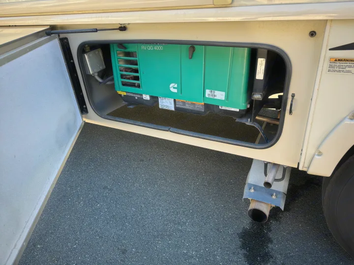An open compartment on an RV rental reveals a green Cummins Onan RV QG 4000 generator with warning labels, parked on asphalt.. Flair-Fleetwood Flair-Fleetwood Motorhome 2017