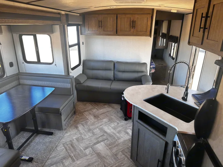 RV rental interior showing a comfortable dinette, large gray sofa, and functional kitchen space.. Keystone RV Springdale 2021