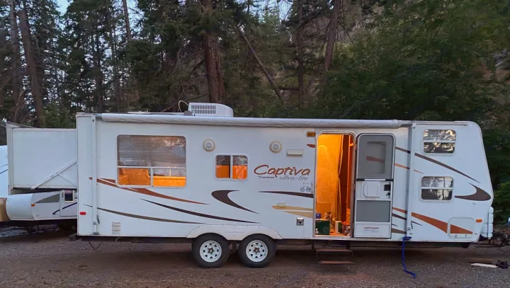 Evening at a peaceful campsite, this Coachmen Captiva RV rental provides warm light amidst the trees for a cozy stay.. Coachmen Captiva 2007