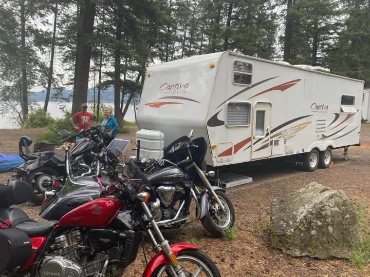 Campsite with a Coachmen Captiva RV, parked next to multiple motorcycles and two people by the lake. Ideal rv rental scene.. Coachmen Captiva 2007