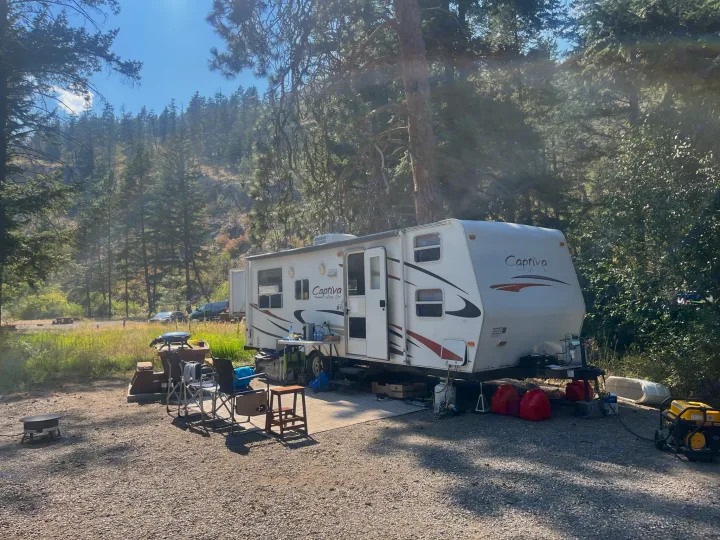 White Captiva ultra-lite RV rental parked at a serene forest campsite with outdoor living setup.. Coachmen Captiva 2007