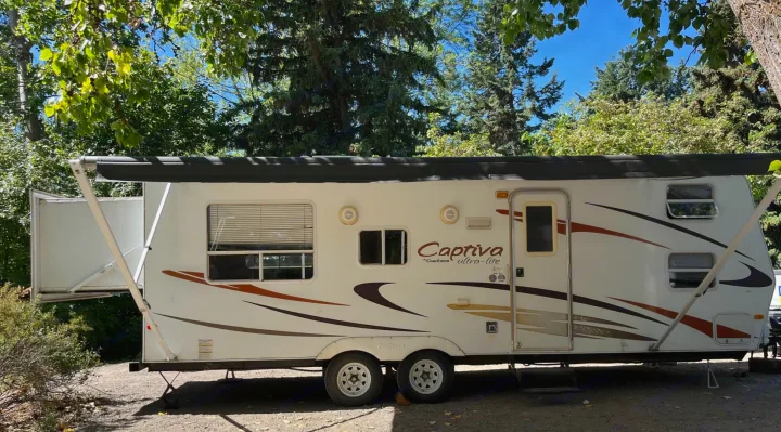 This white Coachmen Captiva ultra-lite travel trailer RV rental is set up in a shaded campsite with its awning extended.. Coachmen Captiva 2007