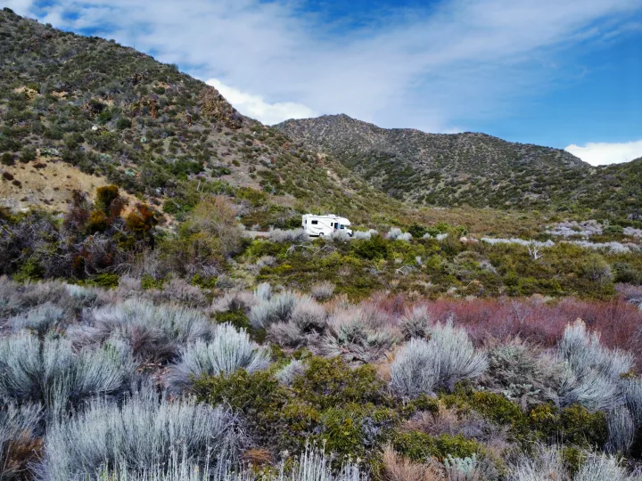 White RV rental parked on a mountain road amidst arid, scrubby landscape under a blue sky.. Thor Four Winds 2019