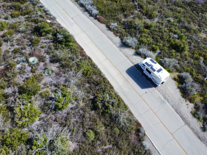 Overhead drone shot of an RV rental with solar panels, parked on a rural road amidst scrubland vegetation.. Thor Four Winds 2019