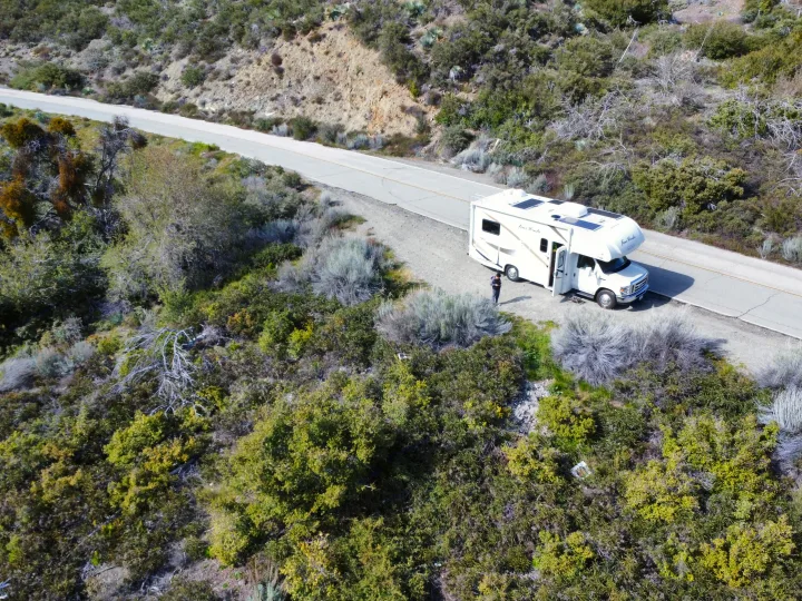 An RV rental, a Thor Four Winds, is parked on a scenic mountain road. A person stands beside it, ready for adventure in nature.. Thor Four Winds 2019