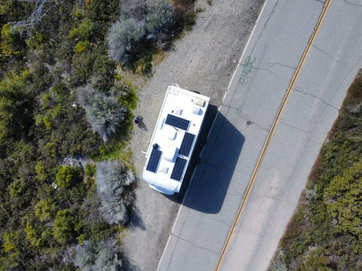 Overhead view: an RV rental with solar panels parked on a dirt shoulder next to a road, surrounded by foliage.. Thor Four Winds 2019