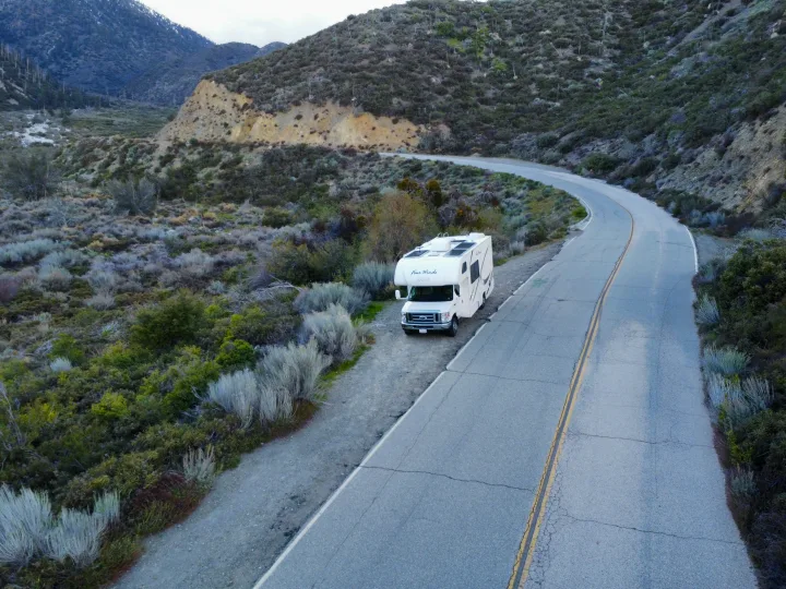 White RV rental parked on a mountain road's dirt shoulder. Winding road through scrubby hills, ready for adventure.. Thor Four Winds 2019