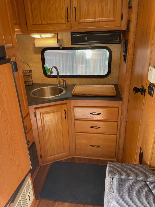 Compact RV rental kitchen/galley with sink, wood cabinets, & window. Ideal for camping trips, perfect for your next adventure.. Four Winds Majestic 2010