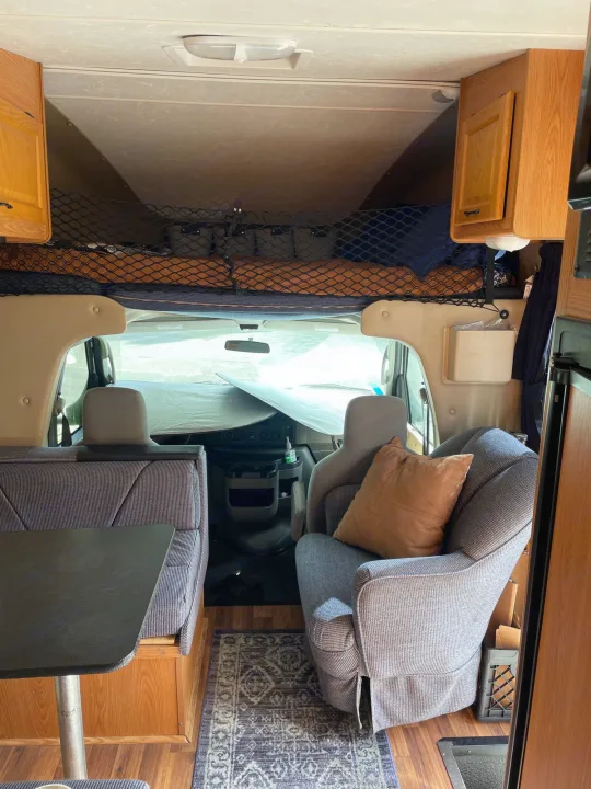 Spacious RV rental interior with an overhead sleeping bunk, dinette, and armchair, ready for comfortable travel.. Four Winds Majestic 2010