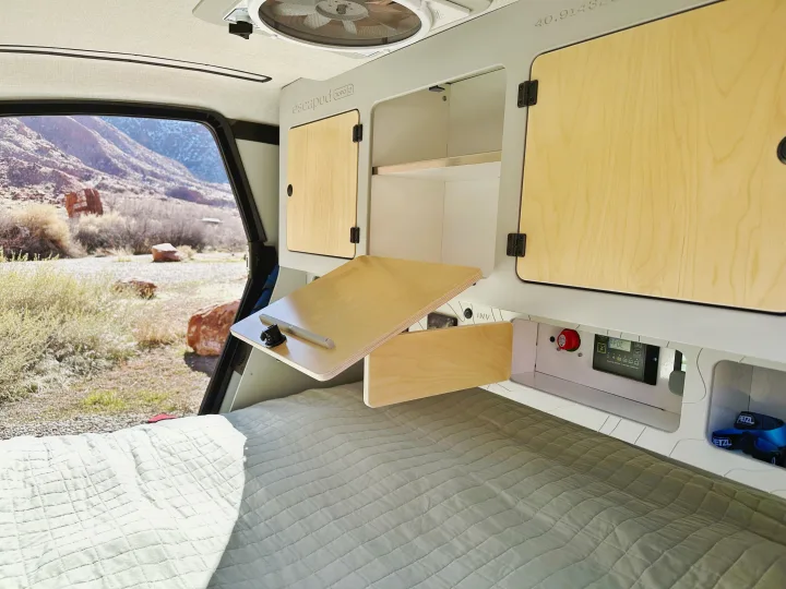 RV rental interior featuring a fold-down desk, bed, storage, power monitor, and scenic desert mountain view.. Escapod Escapod Trailer 2023