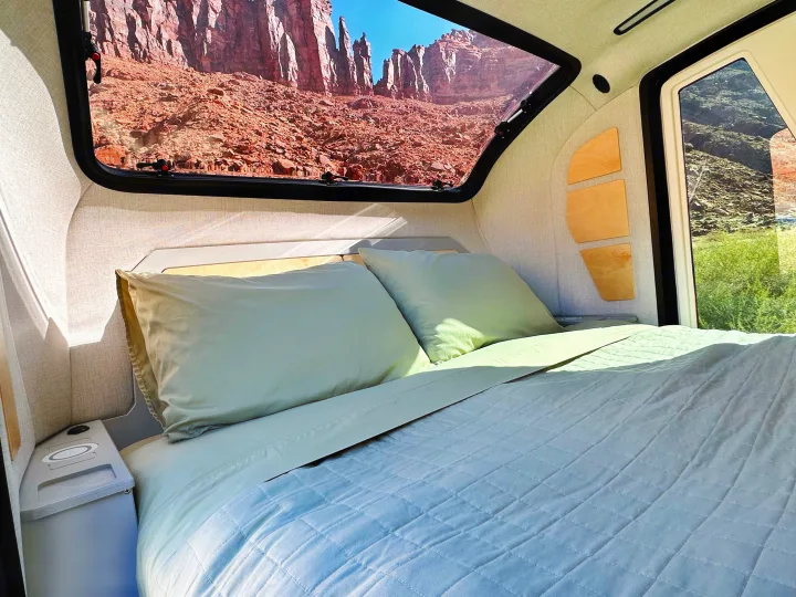 Enjoy nature with this RV rental. Comfy bed inside a camper, featuring a panoramic window view of stunning red rock desert.. Escapod Escapod Trailer 2023