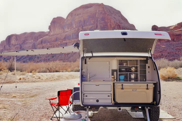 White rv rental camping trailer with its rear open, revealing a full outdoor kitchen, cooler, and sink in a desert landscape.. Escapod Escapod Trailer 2023