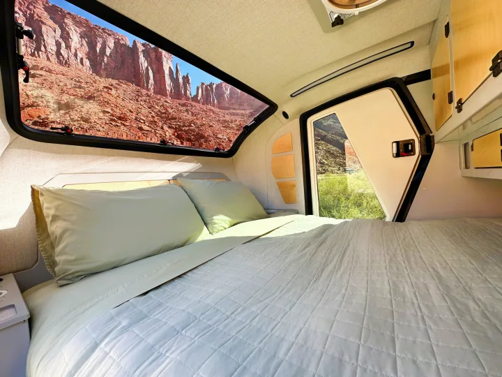 Inside a spacious RV rental: a comfy bed with soft pillows, offering panoramic views of red rock cliffs and a green valley.. Escapod Escapod Trailer 2023