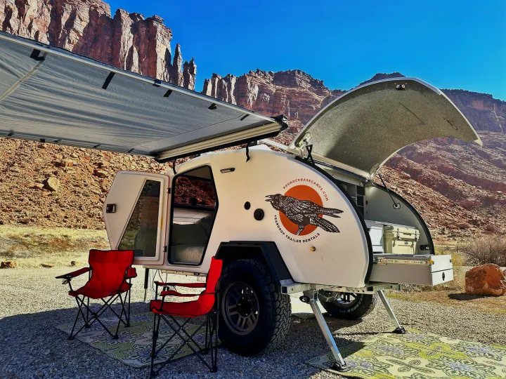 White teardrop trailer RV rental parked with awning & chairs in front of stunning red rock desert cliffs.. Escapod Escapod Trailer 2023